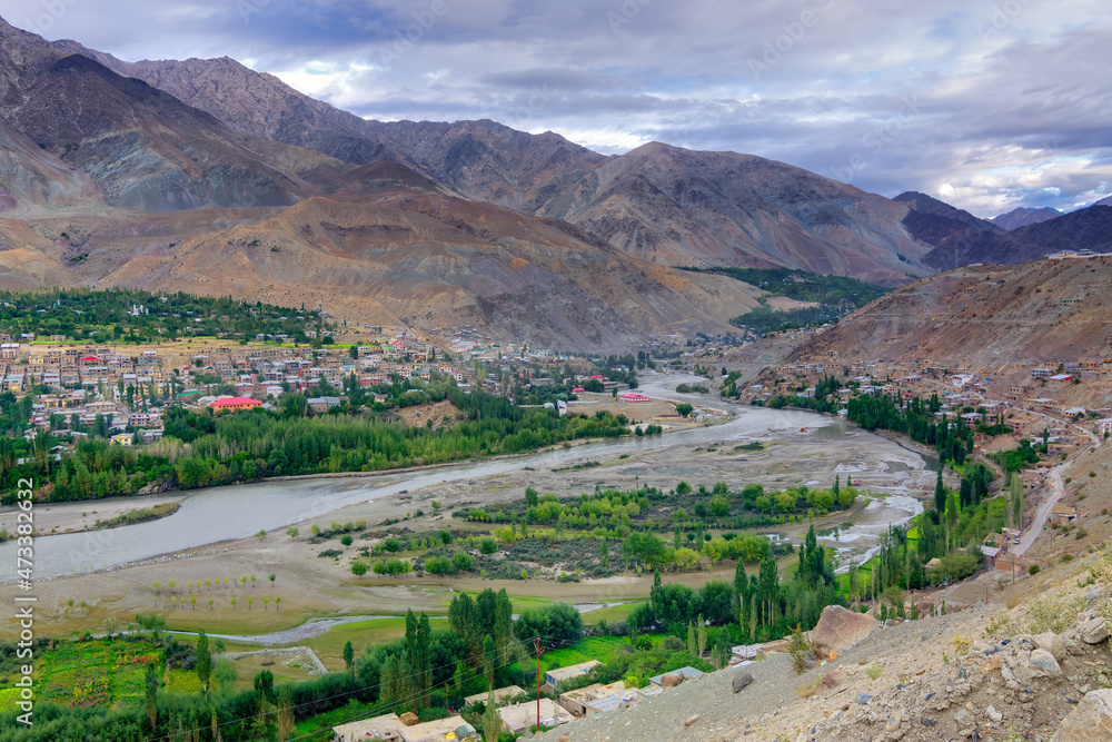 Top view of Indus river and Kargil City valley with Himalayan mountains and blue cloudy sky in background, Leh, Ladakh, Jammu and Kashmir, India Top view of Indus river and Kargil City valley with Himalayan mountains and blue cloudy sky in background, Leh, Ladakh, Jammu and Kashmir, India