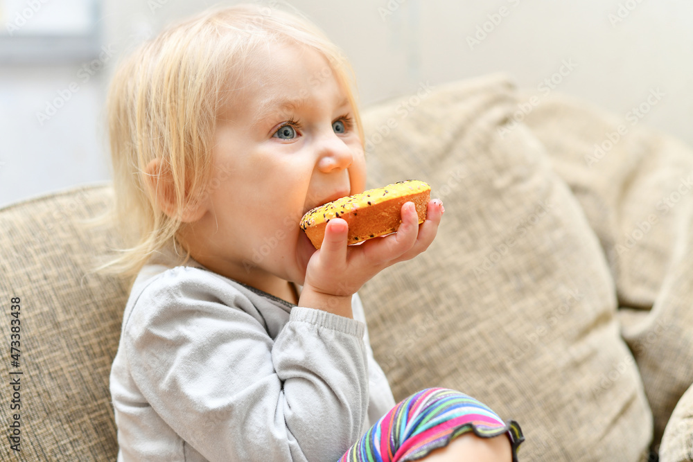 Little child eating a donut with frosting while sitting on the couch. Little child eating a donut with frosting while sitting on the couch.