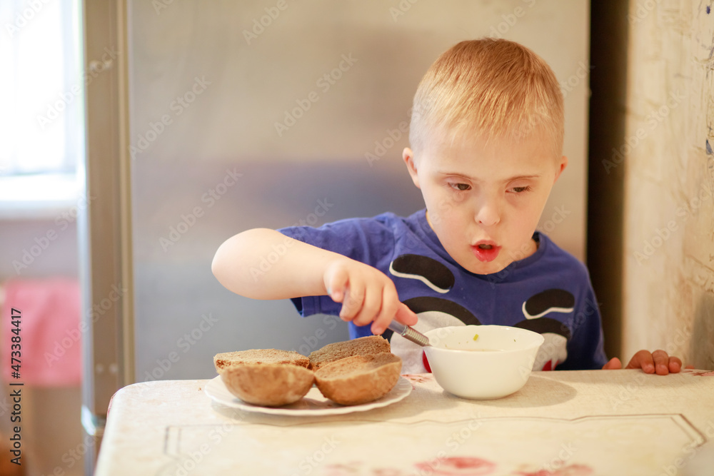 A little boy with a genetic disease Down Syndrome is sitting at the table and eating. The child himself holds a spoon. A special kid eats breakfast.
A little boy with a genetic disease Down Syndrome is sitting at the table and eating. The child himself holds a spoon. A special kid eats breakfast.