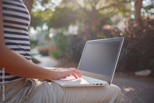 Female hands on laptop, woman types on keyboard sitting in park. Working outside and freelance concept, distance learning