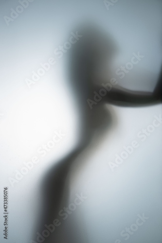 Beautiful and sexy woman stands naked behind a diffuse glass wall in bathroom.
