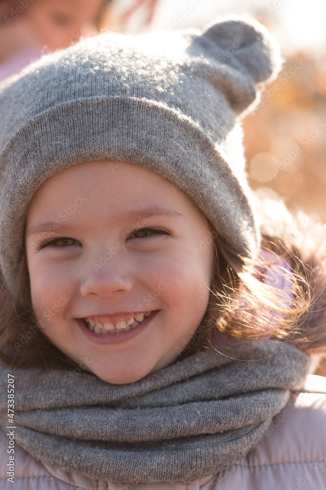 A small beautiful child with a wide smile in a funny hat, a fluffy hood, and a scarf holds a parent's hand on a walk outdoors A small beautiful child with a wide smile in a funny hat, a fluffy hood, and a scarf holds a parent's hand on a walk outdoors