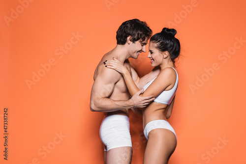 side view of happy and sexy couple in white underwear standing on orange.