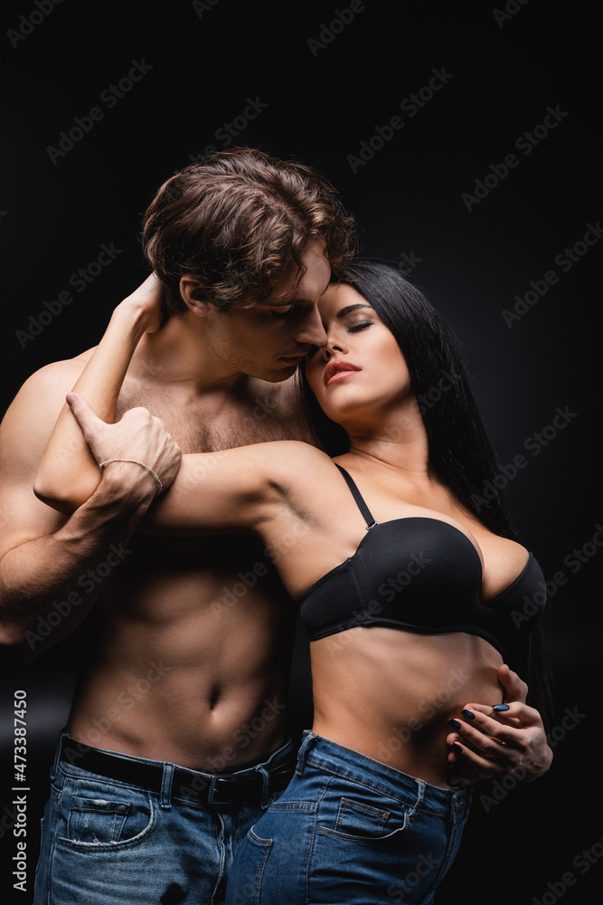 brunette woman in bra hugging shirtless boyfriend on black. brunette woman in bra hugging shirtless boyfriend on black.