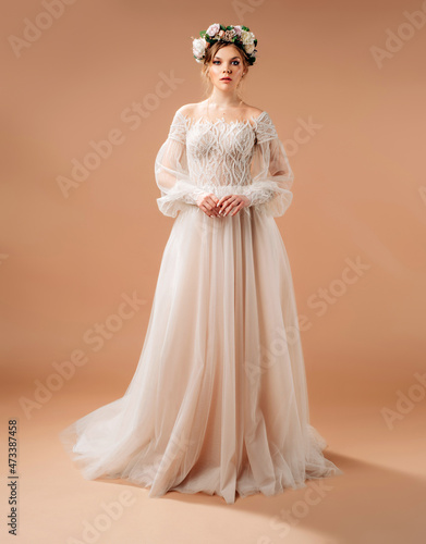 Bridal gown fashion. Beautiful bride in a floral wreath. Full-length portrait in studio with brown background.