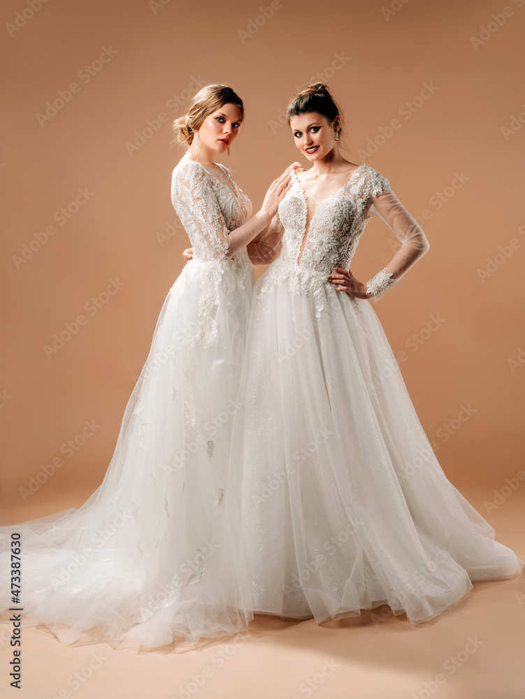 Wedding gown fashion. Beautiful happy brides with smile and long white wedding dresses posing in beige studio. Full-length portrait with neutral background. Wedding inspiration. Wedding gown fashion. Beautiful happy brides with smile and long white wedding dresses posing in beige studio. Full-length portrait with neutral background. Wedding inspiration.