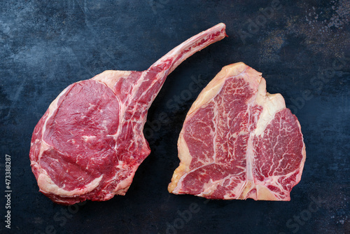 Two raw dry aged wagyu porterhouse and tomahawk beef steaks offered as close-up on a rustic board with copy space
