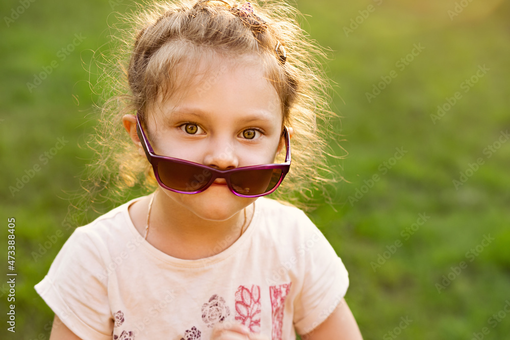 Fun kid girl in sunglasses on green glass outdoor summer background. Closeup Fun kid girl in sunglasses on green glass outdoor summer background. Closeup