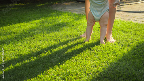 Closeup of little baby feet standing on mother at green grass lawn