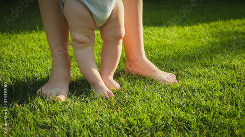 Closeup of adult and baby feet standing on fresh green grass lawn at park on sunny summer day