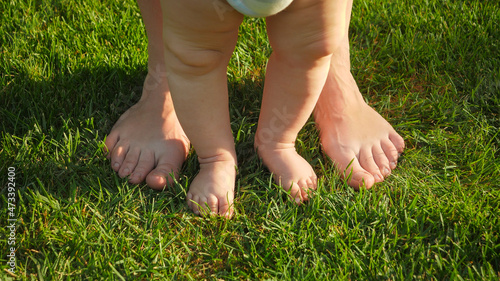 Closeup of tiny baby and big adult feet standing together on grass at hot sunny summer day