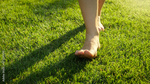 Closeup of adult feet walking on fresh green grass against sunset light
