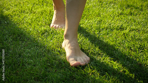 Closeup of barefoot woman walking on fresh green grass lawn.