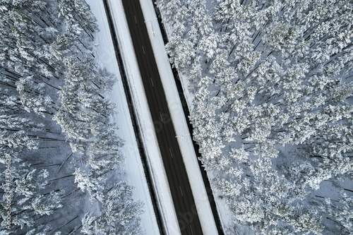 Aerial view of asphalt highway leading through frosty winter forests and groves covered with hoarfrost and snow. Drone photo of black road line and trees with chill snow in mountains. Christmas theme © Defree