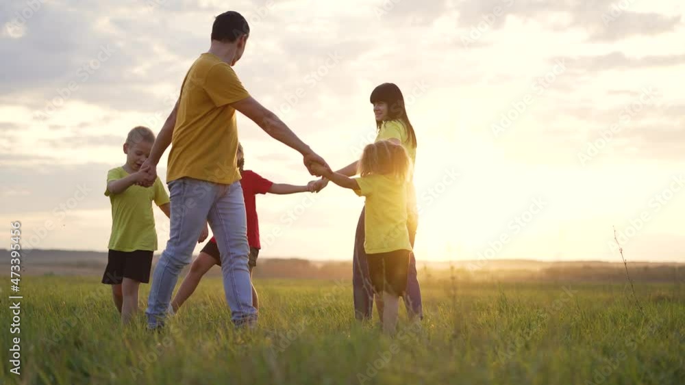 Happy family concept. Group of people hold hands in round dance. Children and parents are play in park on grass. Active lifestyle concept Family on green grass. Happy children play round dance in park Happy family concept. Group of people hold hands in round dance. Children and parents are play in park on grass. Active lifestyle concept Family on green grass. Happy children play round dance in park
