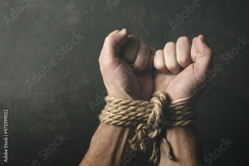 Male hands tied with a rough rope at the wrists close-up on a dark background, soft focus Fototapeta