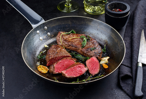 Traditional fried dry aged bison beef rump steaks with herbs and garlic served as close-up in a rustic metal skillet