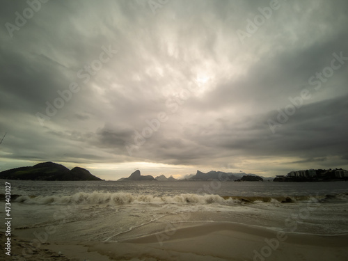 Beach before the storm. Sky with many tropical rain clouds and few people in the distance. Mountains of Rio de Janeiro city on the horizon.