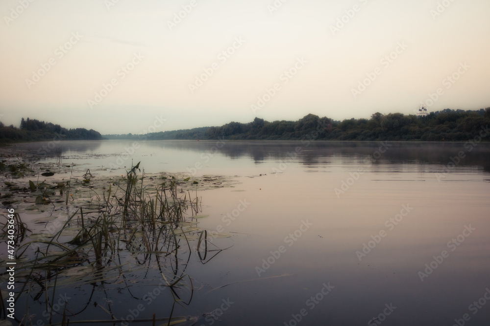 Morning scenery with a calm river and fog on the water and trees on the bank at sunrise
