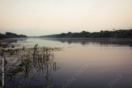 Morning scenery with a calm river and fog on the water and trees on the bank at sunrise