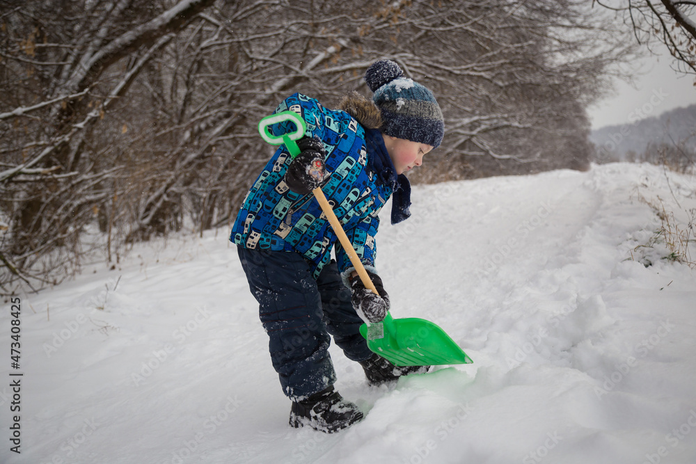 A little boy digs snow with a green shovel. A little boy is playing with snow.
