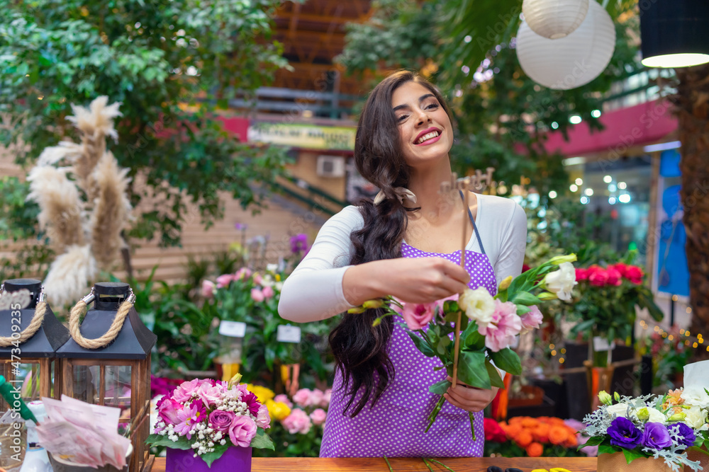 Florist woman working in a flower shop and standing at a counter and making a bouquet of fresh flowers