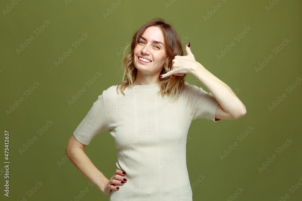 Call me gesture. Positive smiling young woman offering contact communication by phone on green studio background Call me gesture. Positive smiling young woman offering contact communication by phone on green studio background