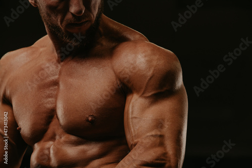 A close-up shot of a torso of a bodybuilder with a beard who is doing bicep curls in a gym. A photo of a part of a muscular man during a workout.