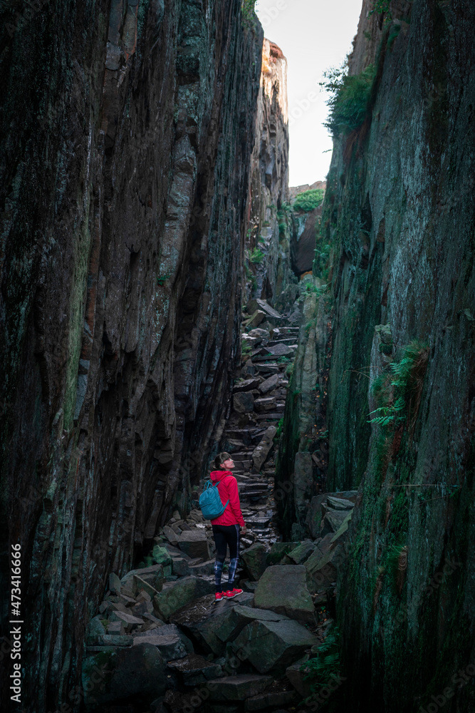 Woman hiking through Kungsklyftan canyon with mossy rocks by village Fjällbacka in Sweden.