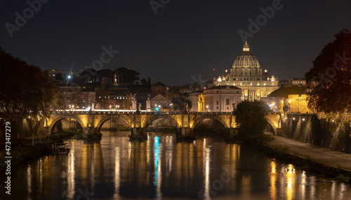 View of the St. Peter's basilica dome with the Vittorio Emanuele II bridge at the foreground, Vatican City, Rome. Light reflection in the water of the Tiber river in the late evening.
