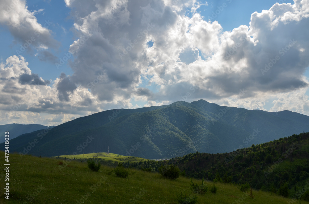 Picturesque landscape with green meadows and forest on hills and mountains at the distance. Carpathian countryside view in summer