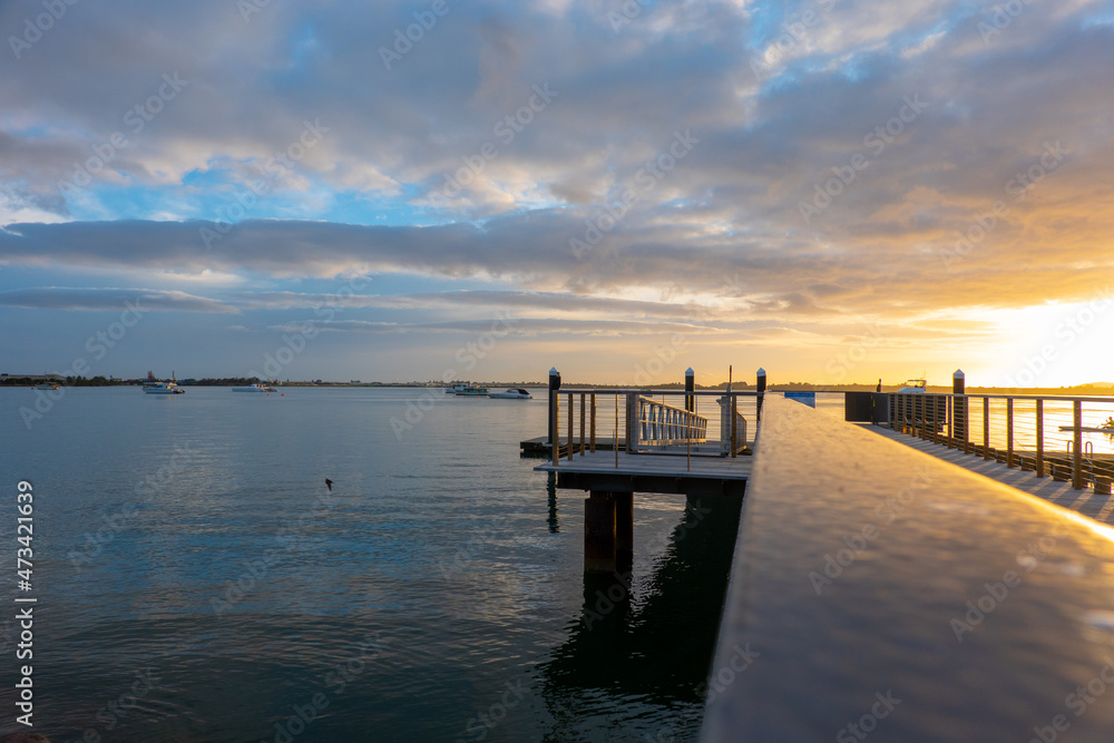 Obraz premium Tauranga waterfront pier and railing reflecting golden glow of morning sunrise.