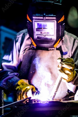 Man welding in a workshop with yellow gloves and black mask photo