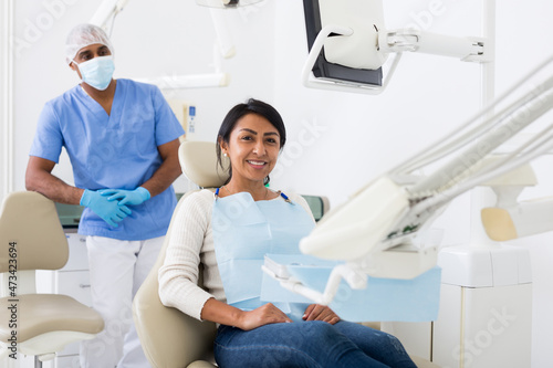 Cheerful hispanic female patient sitting in dental chair waiting for medical examination photo