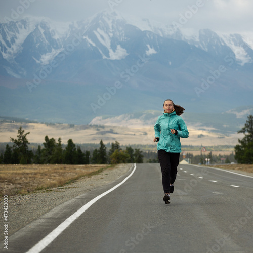 Sports girl is engaged in jogging on the highway against the background of mountains