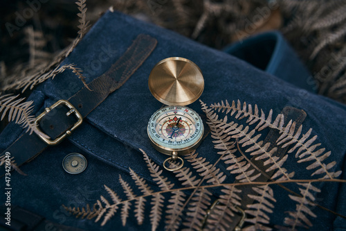 Antique gold compass on top of a backpack in nature to guide the way to the treasure. photo