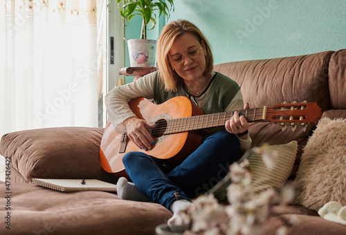 Middle-aged woman plays guitar on the sofa in the living room at home photo