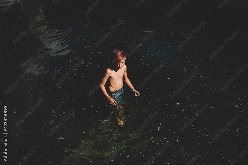 Tween Boy With Pink Hair Stands in a Swirl of Dark Water Tween Boy With Pink Hair Stands in a Swirl of Dark Water
