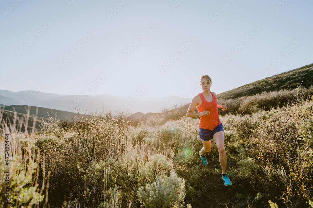 Athletic blonde woman trail runs in the mountains at golden hour Athletic blonde woman trail runs in the mountains at golden hour