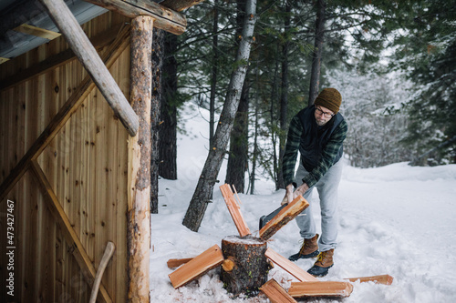A man wearing flannel shirt chops firewood outside in the snow photo