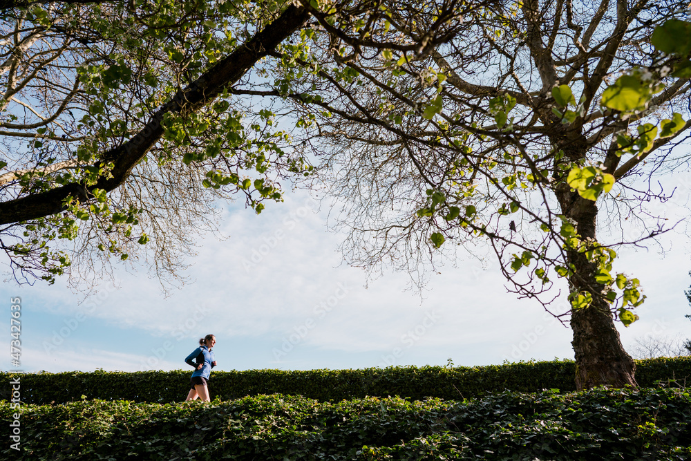 Young woman runs underneath tall green trees and blue skies Young woman runs underneath tall green trees and blue skies