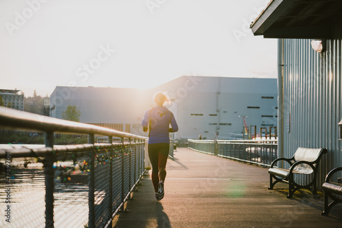 Woman runs into golden light in early morning on urban paved path