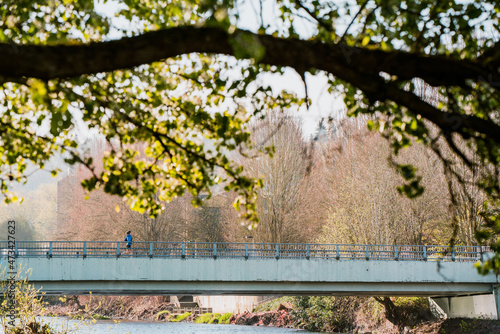 Woman run on bridge over small river with trees in the foreground photo