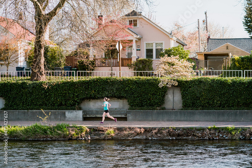 Young woman runs alongside river with houses and trees in background