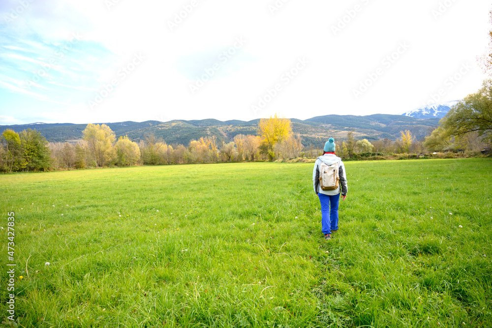 Rear view of a backpacker woman walking on green meadow. Rear view of a backpacker woman walking on green meadow.