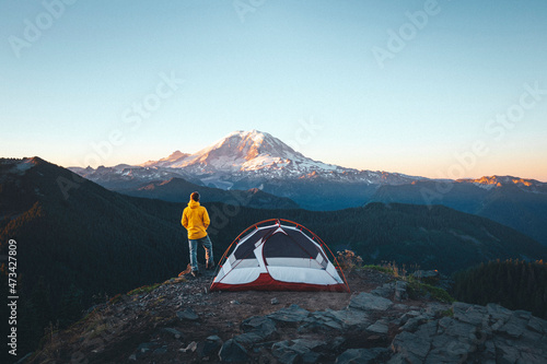A man is standing by a tent on the top of a mountain near mt. Rainier