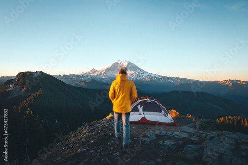 A man is walking to a tent on the top of a mountain near mt. Rainier