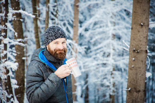 man drinking hot tea in winter forest photo