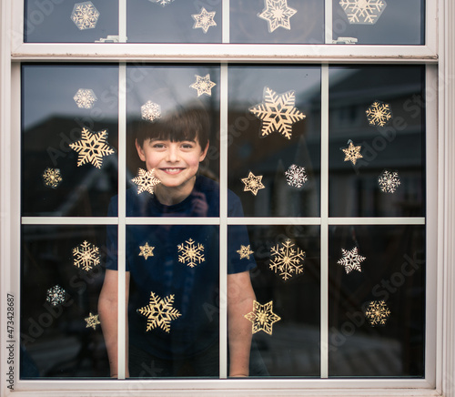 Happy boy looking out through a window covered in snowflake decals. photo