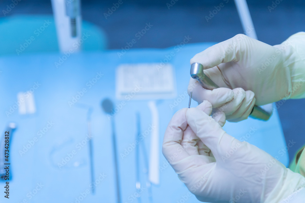 Dentist with gloves on hands preparing the drill in dental clinic Dentist with gloves on hands preparing the drill in dental clinic